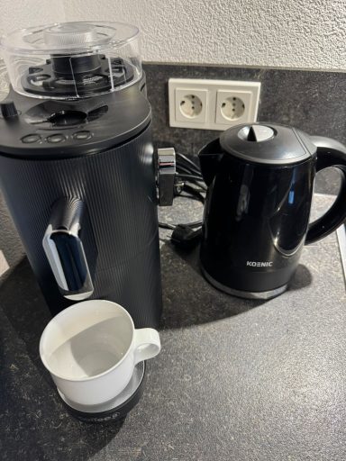 Küchengeräte: Kaffeemaschine und Wasserkocher neben einer weißen Tasse.