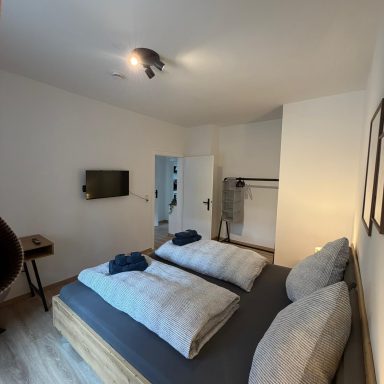 Helles Schlafzimmer mit zwei Betten, Fernseher und offener Garderobe.