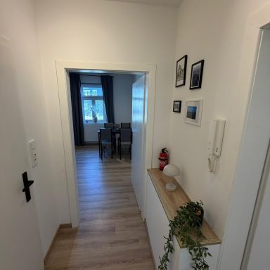 Ein heller Flur mit Möbeln, Bildern an der Wand und Blick auf einen Wohnbereich.