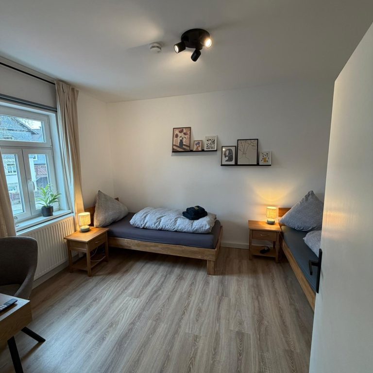 Helles Zimmer mit zwei Betten, Schreibtisch und zwei Nachttischen.
