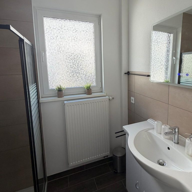 Helles Badezimmer mit Duschkabine, Fenster und modernen sanitären Einrichtungen.