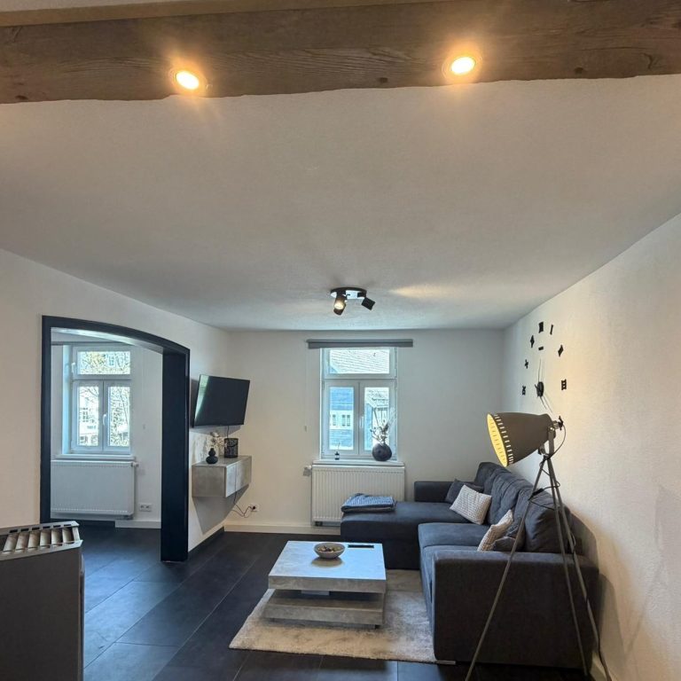 Moderner Wohnraum mit Sofa, Tisch, Fernseher und dekorativem Licht.