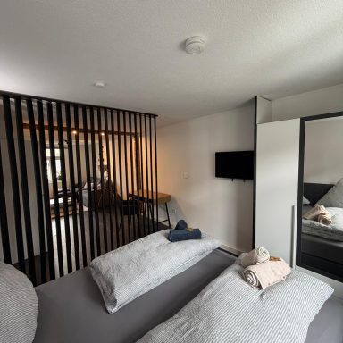 Gemütliches Schlafzimmer mit Doppelbett, schwarzen Trennwänden und angrenzendem Wohnbereich.