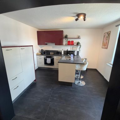 Moderne Küche mit Kochinsel, Stühlen, Schränken und schwarzen Fliesenboden.