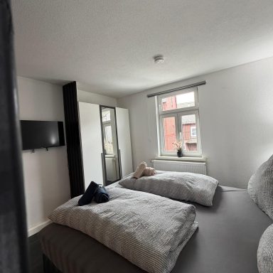Helles Schlafzimmer mit zwei Betten, Fernseher und einem großen Kleiderschrank.