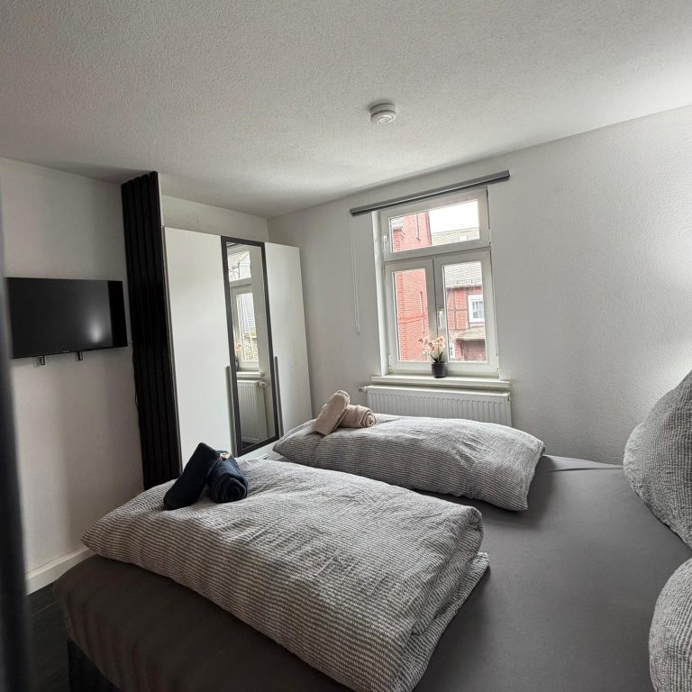 Helles Schlafzimmer mit zwei Betten, Fernseher und einem großen Fenster.