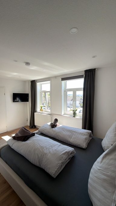 Schlafzimmer Helles Schlafzimmer mit zwei Betten, Fenstern und einem Fernseher an der Wand.