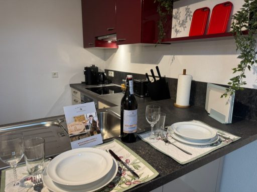 Küche mit gedecktem Tisch, Rotweinflasche und Küchengeräten auf der Arbeitsfläche.