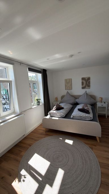 Schlafzimmer Helles Schlafzimmer mit Doppelbett, zwei Fenstern und einem runden Teppich.