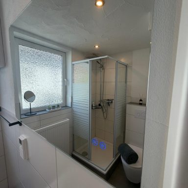 Moderne Dusche in weißem Badezimmer mit Glasabtrennung und hellem Licht.