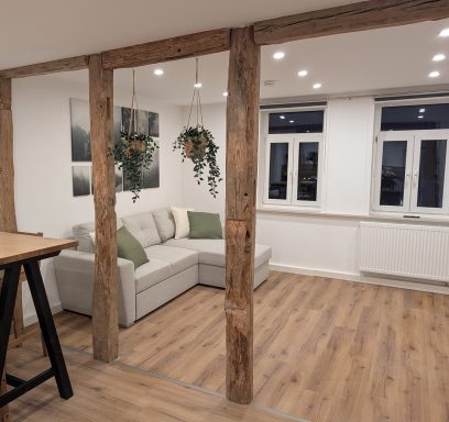 Wohnbereich Heller Raum mit einer L-förmigen Couch, Holzbalken und Pflanzenhängern.