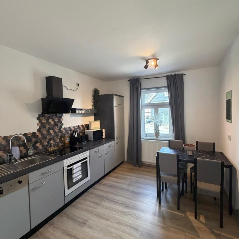 Moderne Küche mit Herd, Kühlschrank und Esstisch, hellem Raum und Fenstern.